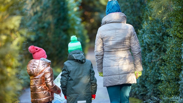 A mum and two children walking through the gardens at Anglesey Abbey with a map in hand, backs to the camera with woolly hats on